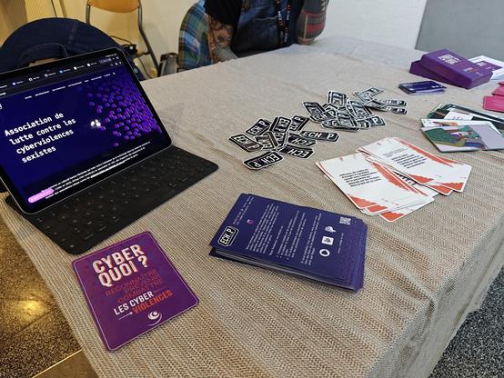 Le stand d'Echap, avec une tablette affichant le site de l'asso, des flyers, des stickers et un jeu de cartes sur les cyberviolences sexistes, le tout sur une nappe sobre mais jolie