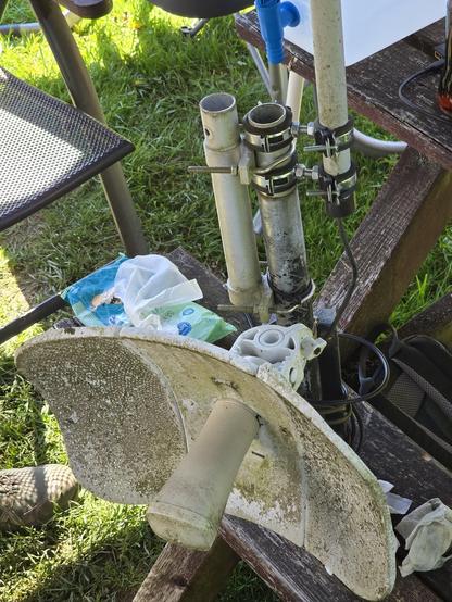 Foto eines UBNT Litebeams an kaskadierender Antennenmast-Erweiterung. Daran ebenfalls eine ADS-B-Antenne. 
Antennen sind veralt/bewittert. Ensemble steht auf einer hölzernen Garten-Bank, darauf Feuchttücher und ein Camping-Wasserkanister.