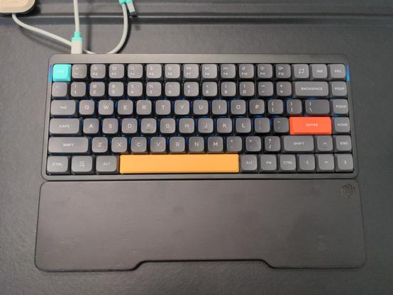 Tastiera meccanica nera con qualche tasto di diverso colore e poggiapolsi nero.