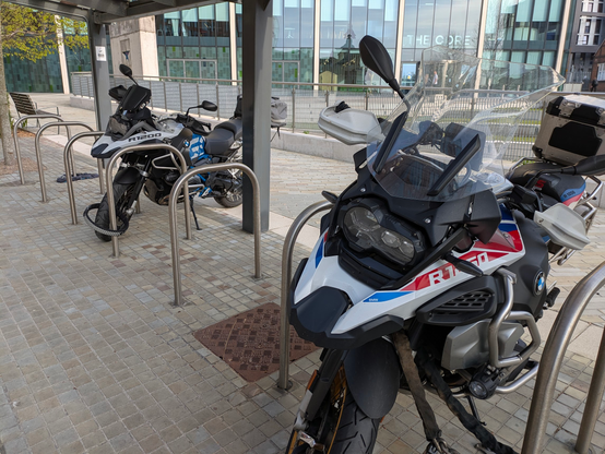 A row of Sheffield stand bicycle racks. There are two very similar motorcycles parked in the racks, both BMW RGS; one a 1200, the other a 1250.