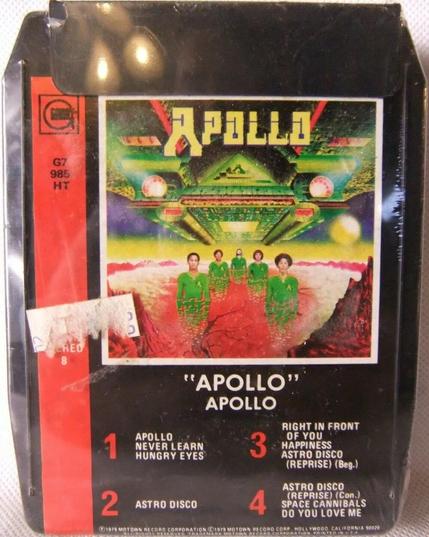 A photo of a vintage black plastic #8TrackCartridge entitled "Apollo" by the band Apollo with some white price-sticker residue left on the cover. Inset artwork shows a drawing of the band wearing green Star Trek-like uniforms standing in formation in a crater of a red planet under a large green and red spaceship. The Gordy record label logo and catalogue number is printed on a vertical red stripe to the left of the image; track titles are printed below.