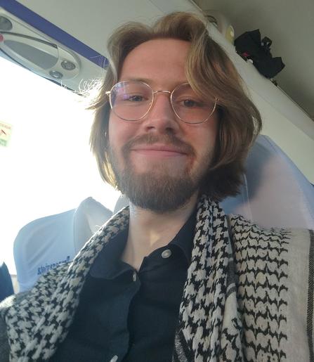 Ein Bild von Erik Uden wie er mit Kufiya in die Kamera lächelt, man sieht das er in einem Bus sitzt