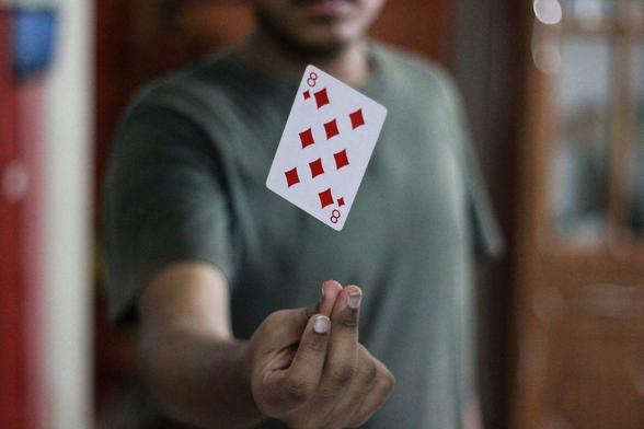 A 8 of diamonds playing card hovers over a person's hand as they snap their fingers. Magic!