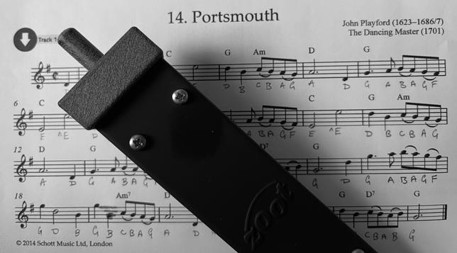 Black and white photograph of sheet music for the tune Portsmouth, from John Playford's 1701 collection The Dancing Master, with my Zoot electronic instrument lying across it. The names of the notes have been pencilled below the musical notation. The Zoot is a long, narrow rectangle, dark grey, with a squarish grey end cap from which a short tube emerges. Several small brass screws are visible in pairs along the body.