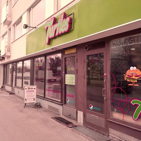 Outside of a pizzeria, with a green facade, and the name "Turtles" above the door in non-copyright-infringing font.