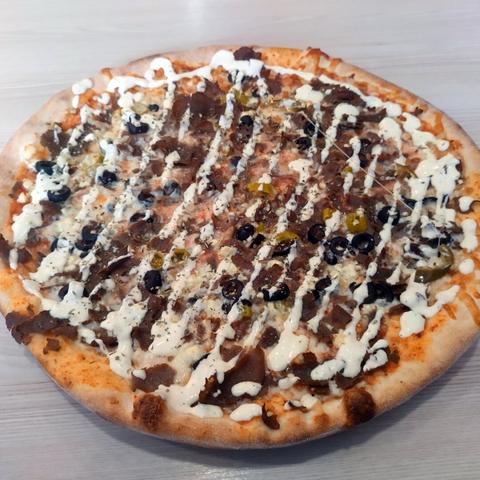 A pizza with kebab meat, olives and green chili peppers, covered with mayonnaise.
