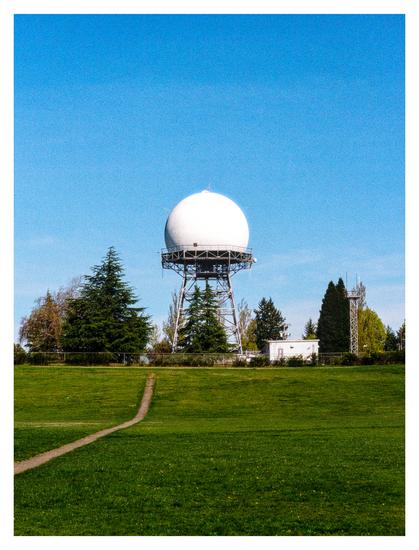 Radar tower in the center of the photo, blue sky above and green lawn in the lower third of the photo.