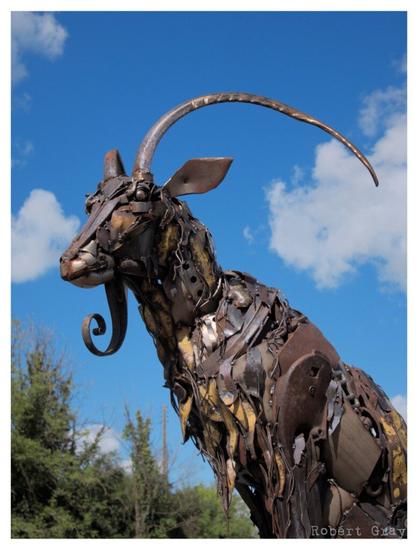 A metal sculpture of a hoat with long horns framed against a blue sky