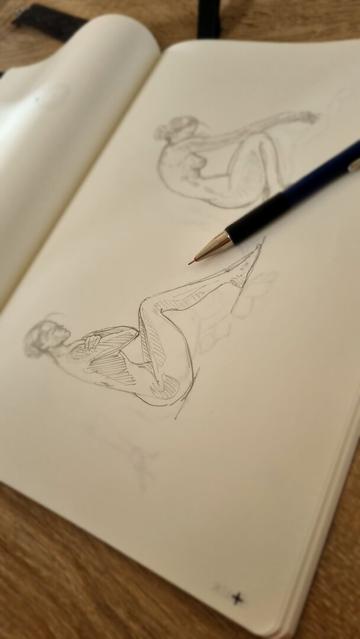 A sketchbook open eith two drawings of a female model and a mechanical pencil