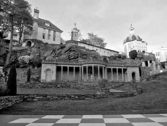 A square decorated with a checkerboard pattern. In the background you can see colonnades and several houses in a rather special style.