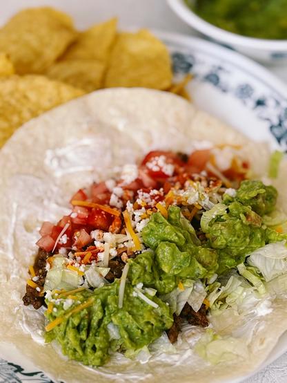 beef taco with tomatoes, lettuce, cheese, rice, guac, sour cream on plate with chips