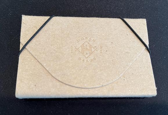 Photo of a nice light brown cardboard business card holder with little elastic straps holding its curved flap closed, and the Hoban Cards logo embossed on the front.