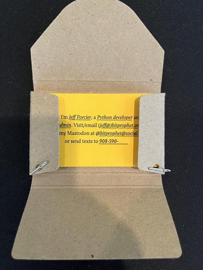 Photo of the business card holder from previous, opened, showing a vibrant yellow-orange business card inside (partly obscured by the side flaps of the holder/box).