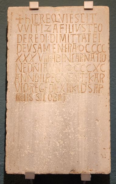 HIC REQUIESCIT/ WITIZA, FILIUS TEO/DEREDI, DIMITTAT EI
DEUS AMEN. ERA DCCCC/ XXXVII, AB INCARNATIO/NE
D(OMI)NI ANNI DCCCXC, ANNO I1 REGNANTE KAR/ULO
REGE, DIE XIIK(AL(EN)D(A)S AP/RELIS. SIC OBIT


Lápida sepuicrai de
marmol con inscripción


Marble tombstone
with inscription


Aqui reposa Vititza, fill de Teodored, que ol senyor al perdoni.
Amen. Va morir el dia 13 de les kalendes d'abril (20 de mare)
de l'any de l'Era (d'August) 938, el 890 de l'Encamació de
Senyor i segon del regnat del rei Carles.


[Aquf reposa Witiza, hijo de Teodoredo, que el sefior lo perdone.
Amén. Murió el dia 13 de las calendas de abril (20 de marzo)
del afio de la Era (de Augusto) 938, el 890 de la Encarnación del
Sefiory segundo del reinado del rey Carlos.

[Here lies Wittiza, son of Theodefred, may the Lord forgive
him. Amen. He died on the 13th day of the calends of April
(20 March) of the year of the Era (of Augustus) 938, in 890 of the
Incarnation of the Lord and second of the reign of king Charles.