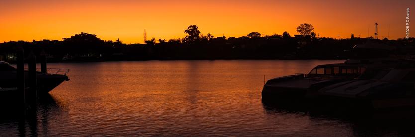 A golden sunrise make a silhouette of the far bank of the Brisbane river as it lights up the sky and river.
