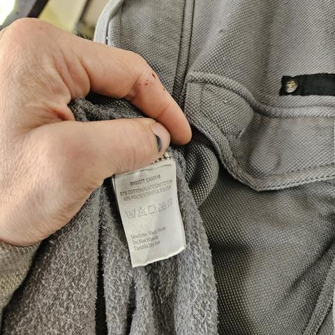 A coat with the tag showing its composition, being 57% cotton 43% polyester. The fabric is grey, a distinct thread raised texture on the outside, fuzz fleece on the inside.