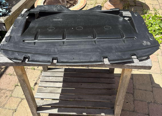 The same under-engine splash shield, removed from my 2003 BMW 5-series station wagon, its now-clean black plastic surface shining in the sun.
