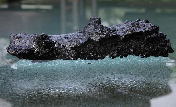A former, completely charred chicken wing, which my spouse accidentally left on the grill, lies on a water covered glass table that is also wet underneath (=> condensation drops, which are only visible in the area where the shadow of said chicken wing falls).