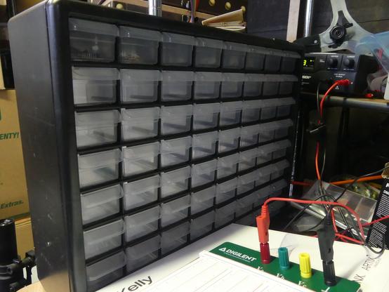 A plastic small parts organizer for electronics parts with a prototyping breadboard in the foreground connected to a power supply.