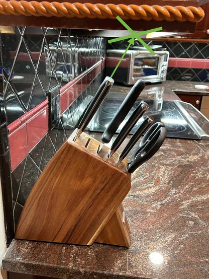 A knife block holds four knives at an angle.  A line shows that the topmost knife would hit the cupboard above if extracted.