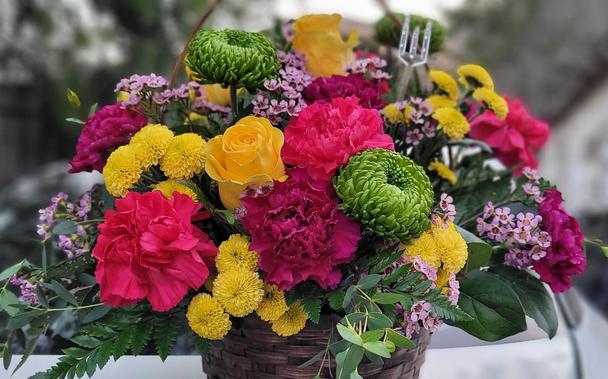 A bouquet with yellow roses, red carnations, green mum's and small purple flowers in a basket