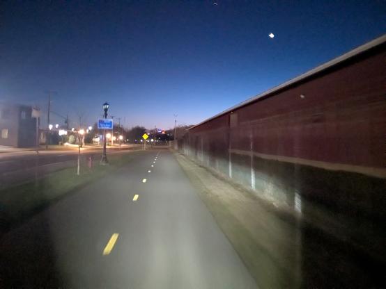 Tar path illuminated by bicycle headlight. A blue sky with moon in the background.