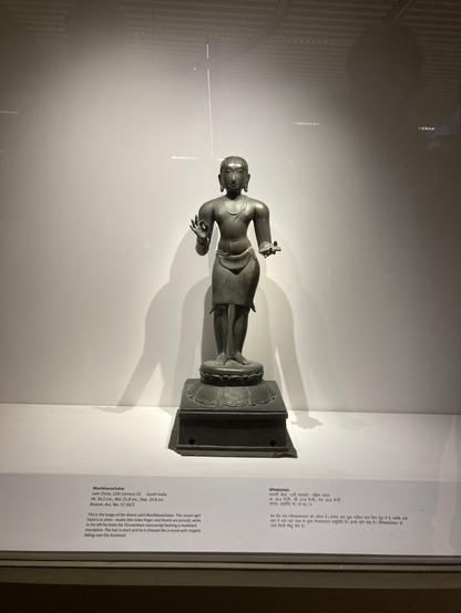 Shaiva saint Manikkavachakar. The raised right hand in china -mudra (the index finger and thumb are joined); while in the left he holds the Tiruvachkam manuscript bearing a mutilated inscription. The hair is short and he is dressed like a monk with ringlets falling over the forehead.