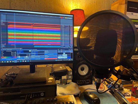 Recording area in basement showing desktop, computer screen, microphone and miscellaneous music item clutter