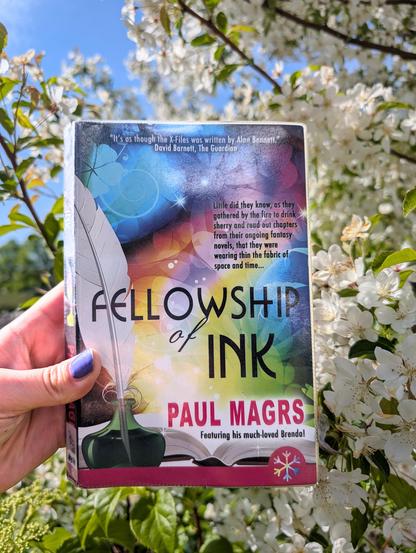 Holding the novel "Fellowship of Ink" by Paul Magrs in front of a blossoming tree