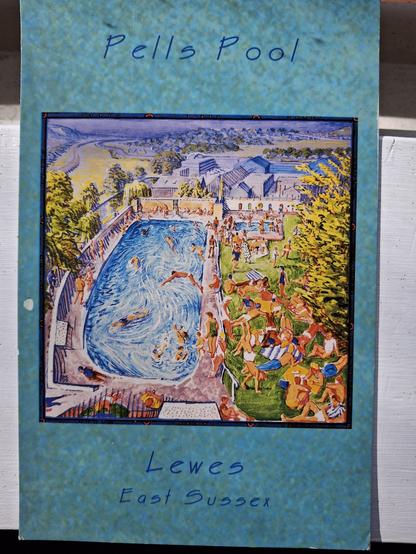 A postcard with an artistic drawing of Pells Swimming Pool, the oldest public swimming bath in Britain. The drawing has people swimming in the pool and relaxing on the grass at the side. There is a border in blue around the drawing with the words Pells Pool, Lewes, East Sussex