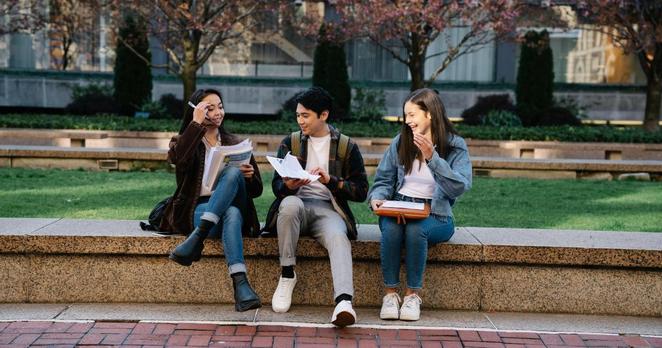 Studierende auf einer Mauer sitzend, unterhalten sich lachend.