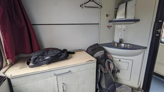 A spacious compartment in a night train. There's a sink, a desk and lots of space for luggage.