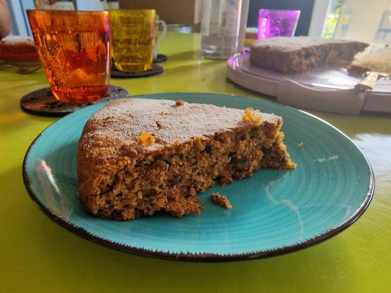 Vollkornmandelbuchweizenleinsamenkarottenwalnusskuchen auf einem Türkisen Teller, bunte Wasser Gläser im Hintergrund