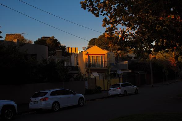 Sunset light hits one house in an otherwise deeply shadowed street under a darkening blue sky