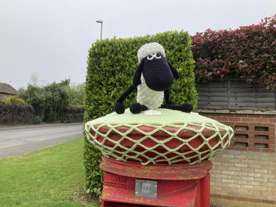 Crocheted Shaun the Sheep atop a traditional red British pillar box