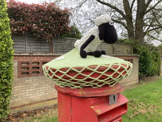 Crocheted Shaun the Sheep atop a traditional red British pillar box