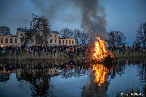A large fire on a raft in a pond, in front of a chateau.