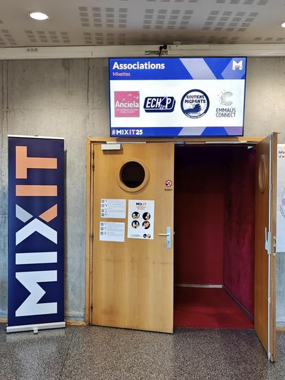 Porte du grand amphi sous un écran qui montre les logos des assos présentes (Anciela, Echap, Soutiens Migrants et Emmaüs Connect) à côté du logo Mixit.