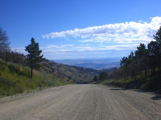 A wide dirt road out of the mountains with a view of the distant of the descent.