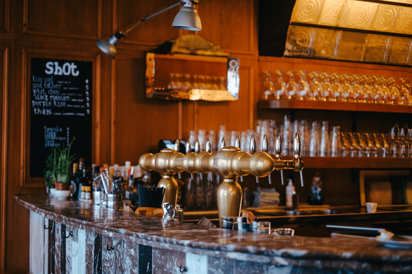The brown marble bar of Kastar, shiny copper coloured taps behind it, in the background wood panelling and glasses on shelves