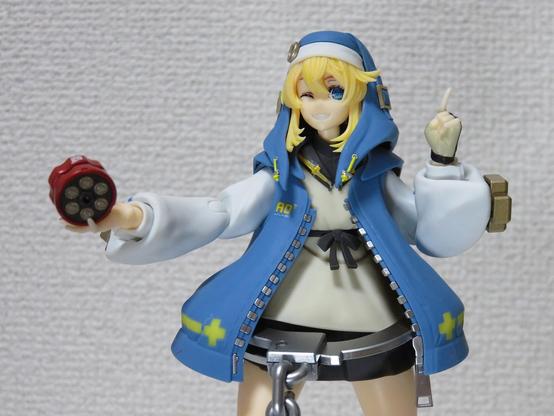 Upper body of a young person with light blue hoodie, beige tunic, black skirt,  abd a huge handcuffs on the waist, holding a red yoyo on the right hand, smiling cheerfully.
A character from the fighting game "Guilty Gear" series.