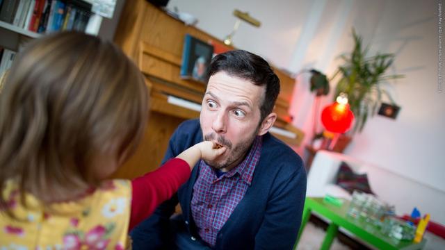 Ein Vater spielt liebevoll mit seiner kleinen Tochter. Sie steckt ihm gerade was zu essen in den Mund. Er schaut sie lustig mit großen Augen an. (Foto: dpa Bildfunk, picture alliance / dpa | Kay Nietfeld)