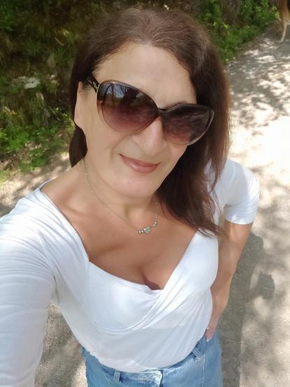 A selfie of a brunette woman in a white top and sunglasses