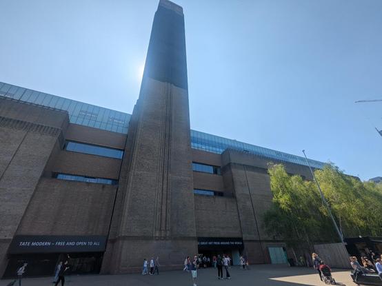 Photo of Tate Modern exterior.  The large phallic tower dominates the image with little people walking around at the base.
