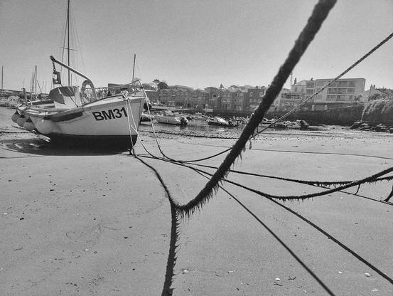 A monochrome (B & W) version ... A seaweed draped rope stretched over a sandy edge of Paignton Harbour, tethering a small fishing vessel.