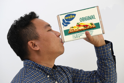 fotomanipulation, ein man mit kurzen schwarzen haaren und einem blau karierten hemd trinkt aus einer wasa original knäckebrotpackung, die er in der linken hand hält, hintergrund ist weiss