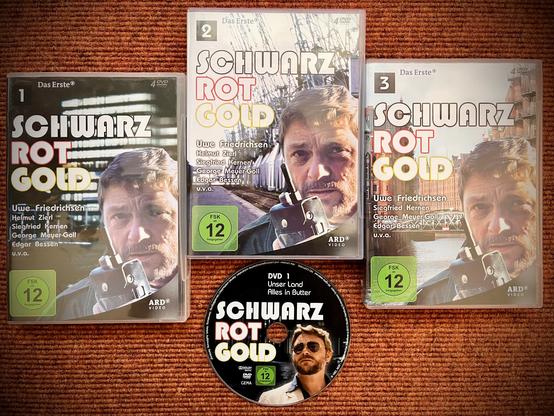 Das Bild zeigt drei DVD-Boxen und eine DVD der Serie "Schwarz Rot Gold". Auf den Covern und der DVD ist neben dem Titel jeweils der Schauspieler Uwe Friedrichsen zu sehen.
