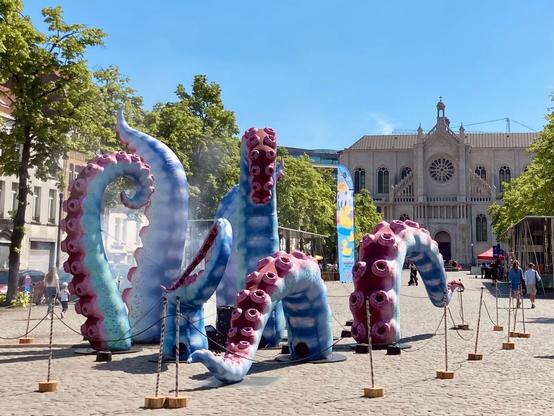 Giant artificial octopus tentacles emerging from the cobblestone surface of the Vismet square, the Saint Catherine church in the background