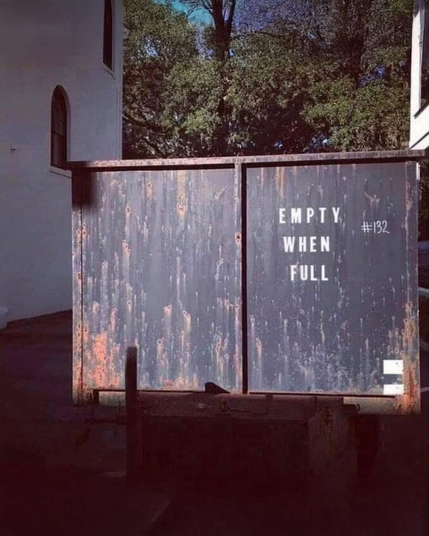 Photo: A dumpster with a stenciled sign on one side which reads, “Empty when full.”