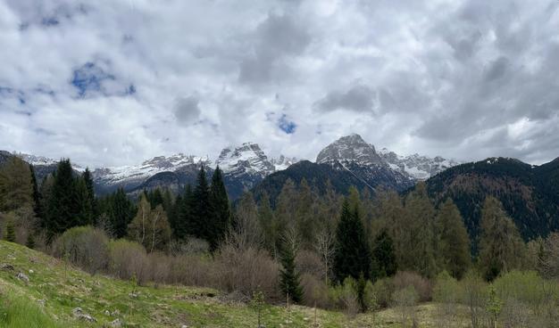 A scenic mountain landscape featuring snow-capped peaks surrounded by lush green forests and a cloudy sky.